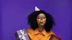 戴着党帽的非洲裔美国女人吹着党的号角，拿着紫色孤立的礼物