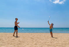 父亲和儿子在沙滩上玩羽毛球拍和羽毛球。家庭度假的概念。海滩上阳光明媚的一天.