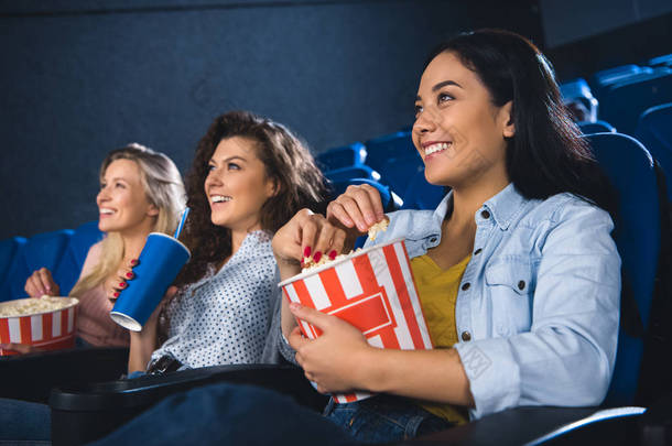 微笑的多种族妇女与爆米花一起看电影在电影院