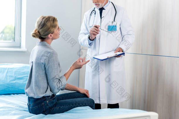 女性病人用手示意, 在医院房间里用剪贴板与男医生交谈