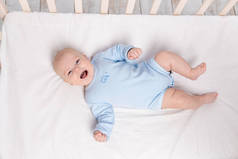 6个月大的可爱的小男孩躺在床上的育婴室里笑着
