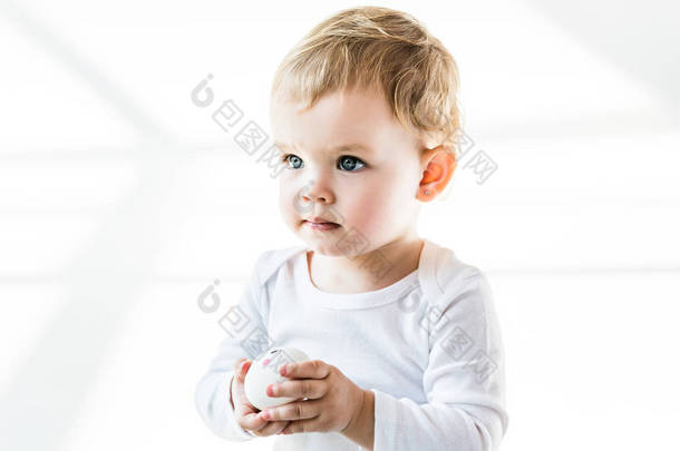 可爱的金发碧眼的婴儿抱着鸡蛋, 看着孤立的白色