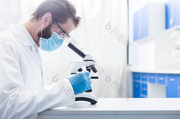 有趣的工作严肃的聪明人坐在实验室里，看着显微镜，而作为一个生物学家