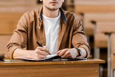 在课堂上, 男生坐在课桌前, 用笔记本写字