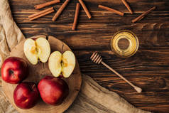木桌上的红色美味苹果、蜂蜜、肉桂和织物的顶视图