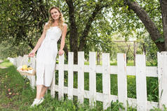 优雅的妇女与水果在柳条篮站在花园的白色栅栏附近