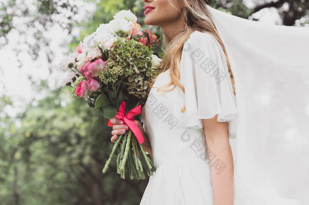 年轻新娘在<strong>婚纱礼服</strong>和面纱上拍摄的照片捧着美丽的花束