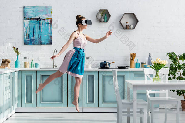 年轻的赤脚女子在空中飞行在虚拟现实耳机和手势在厨房