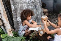 卷曲非洲裔美国儿童在笔记本上写作时的选择性焦点接近贫穷的兄弟玩软玩具