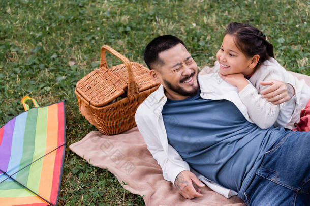 Happy asian dad lying near daughter and wicket basket in park