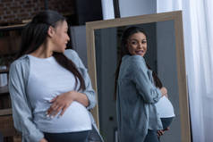 非洲裔美国人怀孕的妇女看着镜子中的倒影