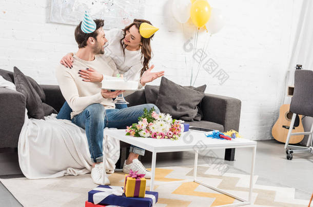 夫妇在党的帽子拥抱和庆祝生日与蛋糕在客厅