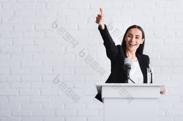 快乐，有吸引力的讲师显示竖起大拇指，而站在讲台上