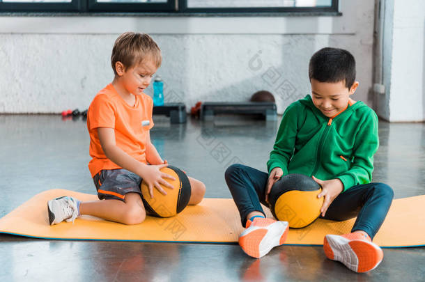 多文化的孩子们在健身房选择性地把注意力集中在手拿球和坐在健身垫上