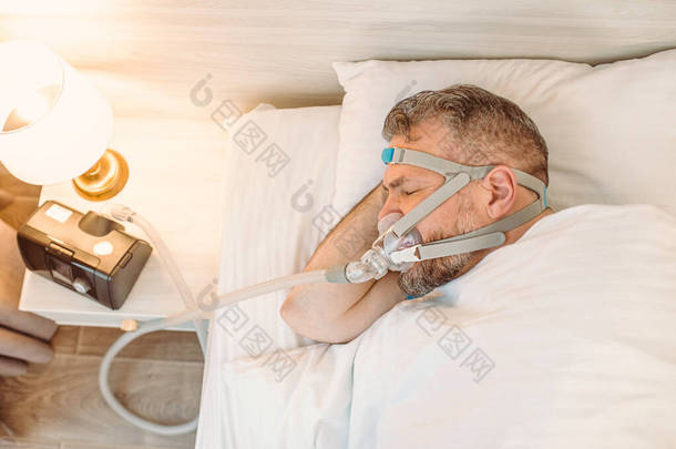 有慢性呼吸问题的<strong>睡眠</strong>男子考虑在床上使用CPAP机。保健、阻塞性<strong>睡眠</strong>呼吸暂停疗法、 CPAP 、打鼾概念