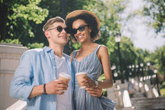 快乐多民族情侣在太阳镜与咖啡杯站在楼梯上公园