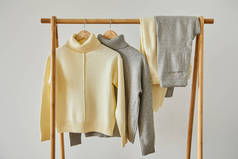 米黄色和灰色针织软毛衣和裤子挂在木制衣架上，与白色隔离