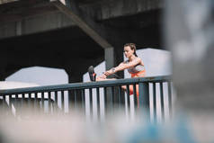 运动女孩伸展腿在栏杆在桥梁