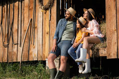 农民家庭头戴草帽，坐在木制谷仓的干草上，望着远方