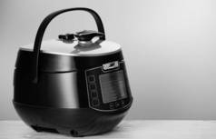 Black modern multicooker, on a white wooden table. With space for text.
