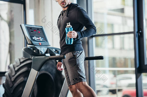 运动员在跑步机上锻炼和拿着运动瓶在健身房的头套的形象