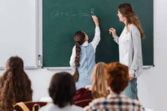在黑板上写字的女学生附近的老师，在模糊的前景上的学生