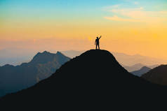 在日落时分，一个手拿着愉快的高举在山顶上的人的轮廓：努力与成功的概念