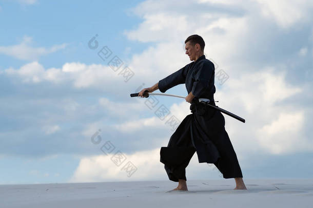 专注的人, 在传统的衣服, 是练习日本<strong>武术</strong>-iaido 在沙漠中与日本剑-一个武士<strong>刀</strong>在日落的背景下的黄昏天空。侧面视图.