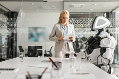 在会议室里，一位迷人的女商人站在机器人旁边，一边用数字平板电脑