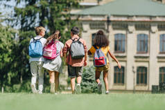 四个多元文化的学童背着背包在公园里草坪上散步的背景