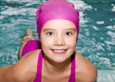可爱的微笑的小女孩游泳在游泳池室内的肖像粉红色的泳衣和帽子
