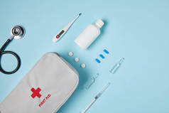白色急救包袋与听诊器和各种药物在蓝色表面的顶部视图