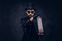 魔术师在黑色的西装, 太阳镜和顶帽子, 显示在黑暗背景下打牌的把戏.