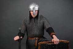 一个中世纪的骑士的画像，他的晚期维京时代和十字军的开始坐在他的膝盖上。戴锁链的骑士，戴着盾牌和剑的头盔，被隔离在黑暗的背景下.