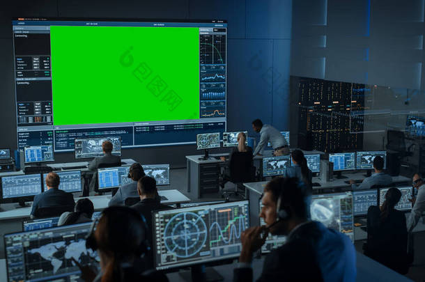 大型绿色屏幕水平造型在飞行控制中心的房间里，有飞行主任和其他在计算机上工作的控制器。在充满展示的监控室工作的工程师小组.