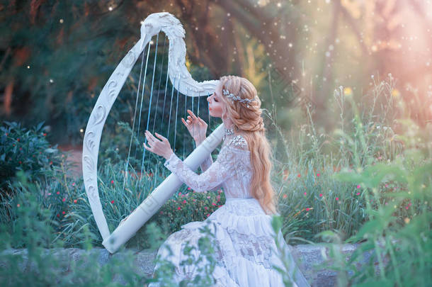 神秘的森林仙女在神话般的地方玩白色竖琴，女孩与长长的金发和优雅的蕾丝复古礼服呼吁明亮的阳光，夫人与<strong>银首饰</strong>和乐器