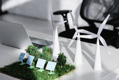 椅子附近的桌子与笔记本电脑, 树木, 风车, 太阳能电池板模型在草地上的办公室