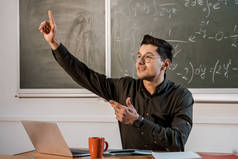 男教师坐在桌旁, 指着空气, 在数学教室里解释方程式