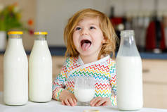 可爱的蹒跚学步的小女孩早餐喝牛奶.可爱的女婴，有很多瓶子。以牛奶为健康钙来源的健康儿童。早上在家或托儿所里的小孩.