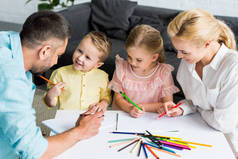 高视角的快乐的父母与可爱的小朋友一起在家里画画
