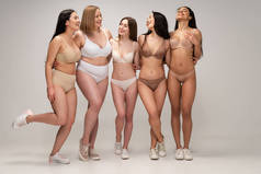五个开朗的多元文化年轻女性在内衣拥抱, 而摆姿势在镜头, 身体积极的概念