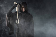前视图的妇女在死亡服装举行悬挂的绞索在烟雾上黑色