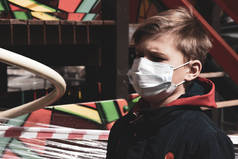 在操场上戴着医疗面具的男孩。用带子包裹的游乐场