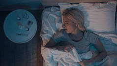 在床头柜边的温度计和药丸旁边睡觉的年轻女子的头像