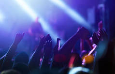 观众举手在音乐节和灯光从舞台上方流下。 群众举手，跳舞，欣赏音乐会.