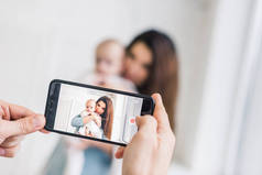 在智能手机上拍摄妻子与婴儿的照片的男子的裁剪拍摄照片