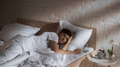 男人睡在床上接近闹钟和床头柜上的盆栽兰花