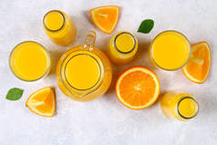 玻璃瓶, 眼镜和一壶新鲜的橙汁与切片橙色和黄色的管在一个浅灰色的表。顶部视图。平躺.