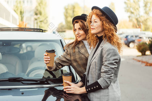 穿着黑帽和夹克的<strong>时尚女性</strong>站在汽车附近的电视在街上的侧视图