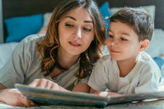 迷人的母亲和快乐的蹒跚学步的男孩看着书本的选择性焦点